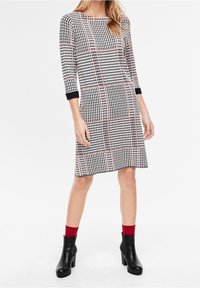 Černobílé kostkované šaty s tříčtvrtečními rukávy, kulatým výstřihem a růžovými akcenty. Doplněné černými botami na podpatku a červenými ponožkami.