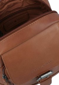 Borsa in pelle marrone con superficie testurizzata, scomparti con zip e chiusura a patta. All'interno presenta un'etichetta del marchio. Design semplice.