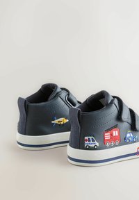 Tumši zili bērnu sporta apavi ar izšūtu dzeltenu lidmašīnu, ātrās palīdzības mašīnu, ugunsdzēsēju automašīnu, policijas auto un sarkano autobusu uz baltām zolēm.