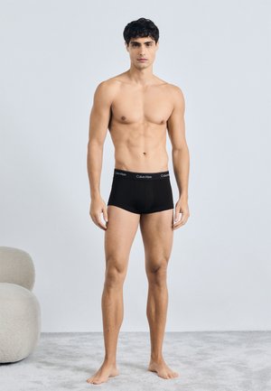 Boxer brief neri in cotone con una morbida vita caratterizzata dal logo "Calvin Klein". Il modello sta in piedi a piedi nudi su un tappeto grigio chiaro.