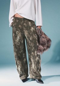 Szerokie zielone spodnie z wzorem liści, miękka tekstura i elastyczny pas, w zestawie z szaro-futrzaną torebką i czarnymi butami na szpilkach.