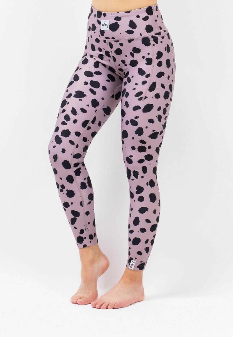 Leggings in a mauve color, featuring a black spotted pattern. High waistband, stretchy fabric, and a logo patch at the ankle.