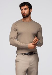 Beige neulepaita kevyessä kankaassa, pitkät hihat, ribbireunat. Yhdistetty beigeihin housuihin ja mustaan vyöhön, kellon korostus.