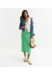 Veste en denim, top blanc à côtes, jupe midi verte à fleurs, baskets crème avec des accents bruns, et un sac tote marron et crème.