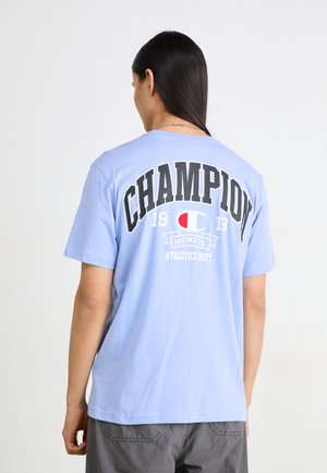 Light blue cotton t-shirt featuring large black "CHAMPION" text on the back, white and red logo, and casual short sleeves.
