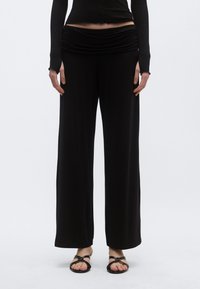 Μαύρο παν τελόνι με φαρδιά γραμμή και ζώνη με drape, κατασκευασμένο από απαλό ύφασμα, με λεία υφή και άνετη εφαρμογή. Φοριέται με επίπεδα σανδάλια.