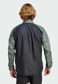 Chaqueta ligera con un cuerpo negro y mangas con un patrón verde, mangas largas ajustadas y un cuello alto para mayor cobertura.