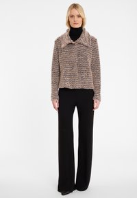 Strickjacke mit breitem Kragen in Beige- und Brauntönen. Lange Ärmel, sichtbare Textur und verkürzter Schnitt, kombiniert mit schwarzen Hosen.