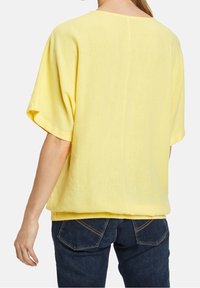 Żółta, krótka bluzka z krótkim rękawem, wykonana z lekkiego materiału, o luźnym kroju i delikatnej fakturze, z okrągłym dekoltem i dołem.
