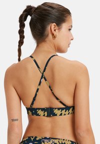 Reggiseno sportivo blu e giallo a fantasia con design a incrocio e gancetto regolabile. Realizzato in tessuto elasticizzato; minimalista e funzionale.