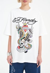 Vit bomull t-shirt med en djärv, färgglad tatueringdesign som innehåller ett kranium, vingar, hjärta och text—"Ed Hardy," "New York," "City."