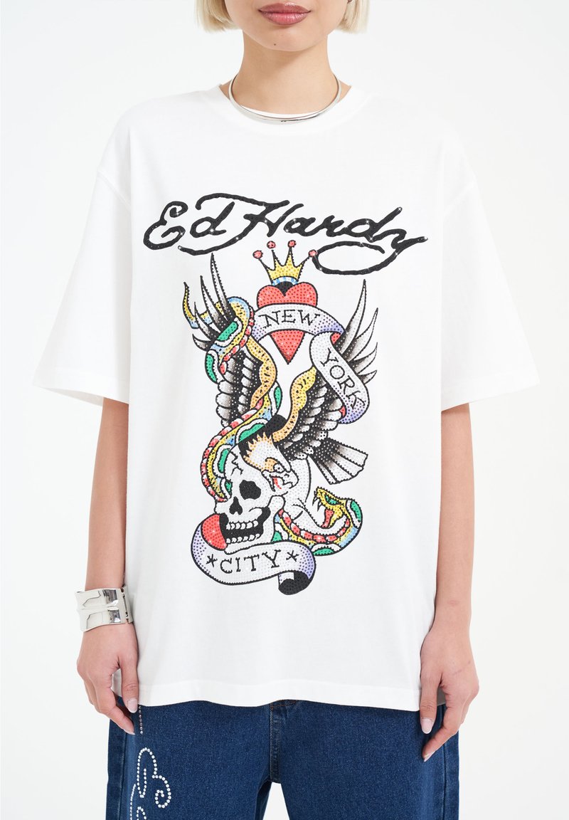 Vit bomull t-shirt med en djärv, färgglad tatueringdesign som innehåller ett kranium, vingar, hjärta och text—"Ed Hardy," "New York," "City."
