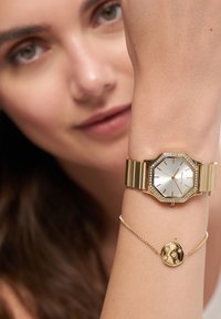 Guld octagonalt ur med en sølv ansigt og krystal udsmykninger, parret med et delikat guld armbånd med en rund charm og små sten.