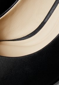 Gros plan sur la surface extérieure lisse d'une chaussure noire et la doublure intérieure rembourrée beige.
