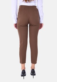 Pantaloni brown attillati con vita alta, caratterizzati da cuciture verticali e indossati con tacchi neri. Texture liscia, design a gamba affusolata.