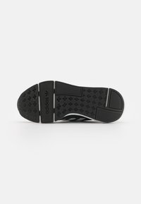 Suola di una scarpa sportiva nera, caratterizzata da gomma texturizzata con un motivo a spina di pesce, tre strisce bianche e un logo sul tallone.