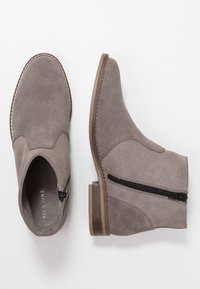 Grey suede ankle boots with a side zipper, textured accents, and a brown rubber sole. Stitch detailing along the edge enhances design.