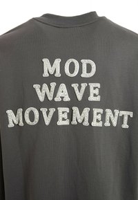 Sudadera gris con letras grandes y texturizadas que dicen "MOVIMIENTO OLA MOD" en la parte posterior, hechas de un material brillante.