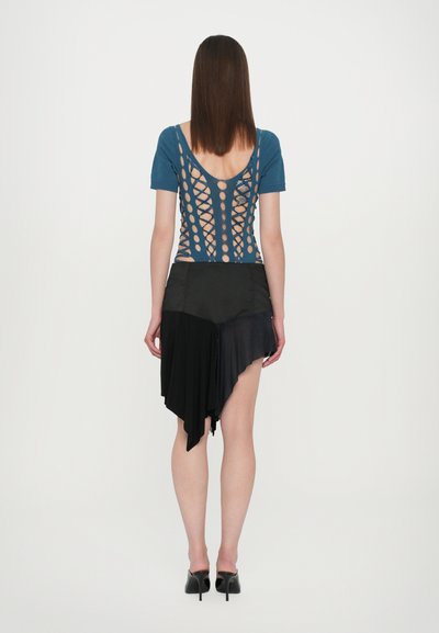 Haut bleu à manches courtes avec un dos croisé ; associé à une jupe noire asymétrique montrant différentes textures de tissu. Talons noirs.