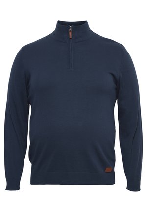 Tumedas sinine kootud aluspluus, mida iseloomustab kõrge krae, tõmblukuga sulgemine ja väike pruun nahklogoga märk ääres.