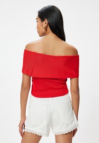 Rød strikket top uden skuldre med ribbet tekstur og bred udskæring, parret med hvide denim shorts med bølget kant og baglommer.