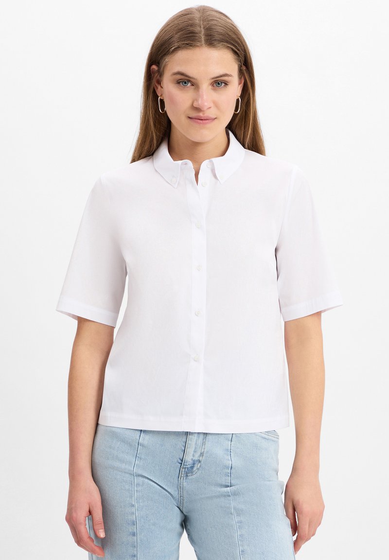 Kurzärmeliges weißes Hemd mit button-down Kragen, mit glatter Textur und geradem Schnitt, kombiniert mit hellblauen Jeans.