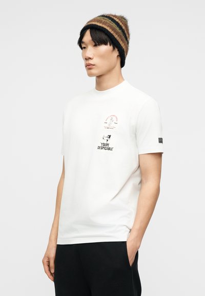 Νέος άνδρας που φοράει λευκό T-shirt με μικρό γραφικό και κείμενο που γράφει «ΕΙΣΑΙ ΑΠΕΧΘΗΣ», καφέ ριγωτή σκουφί και μαύρο παντελόνι.