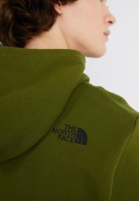 Felpa verde con cappuccio realizzata in morbido tessuto, con un piccolo logo nero di "The North Face" sulla spalla destra.