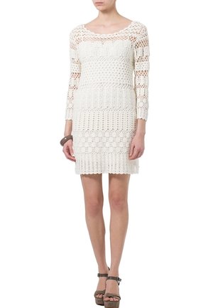 White crochet dress with three-quarter sleeves, featuring detailed patterns and a fitted silhouette, complemented by heeled sandals.