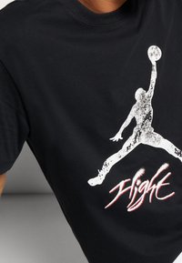 Černé bavlněné tričko s bílou grafikou skákající postavy a nápisem "Flight" v červeném písmu níže. Klasický design s kulatým výstřihem.