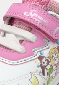 Nærbilde av rosa og hvite barne sneakers med "Havfrue-magi" stropp og fargerike havfrueillustrasjoner på siden.