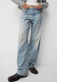 Light blue wide-leg jeans in faded denim with a high waist and contrast stitching, paired with dark brown heeled boots.
