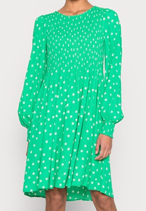 Zielona sukienka z białym kwiatowym wzorem, długimi rękawami i marszczoną górą. Zwiewna tkanina o lekkim kształcie trapezu, długość do kolan.