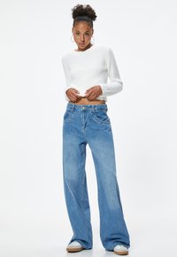 Witte, gek textureerde cropped sweater gecombineerd met blauwe, high-waisted wijde jeans met voorkruiden en zichtbare stiksels.