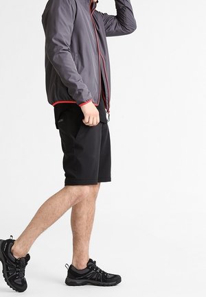 Chaqueta gris con detalles en rojo, pantalones cortos negros y zapatillas negras. Tela suave, ajuste atlético y bolsillos laterales en la chaqueta.