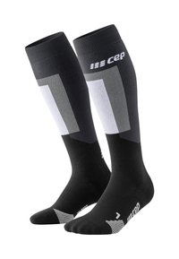 Calze compressive nere con un design che presenta accenti grigi e bianchi, tessuto a maglia, bordo a coste e dettagli decorativi nella zona dei piedi.