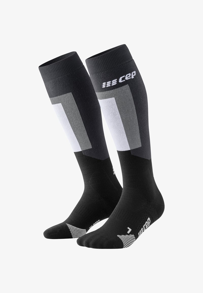 Calze compressive nere con un design che presenta accenti grigi e bianchi, tessuto a maglia, bordo a coste e dettagli decorativi nella zona dei piedi.