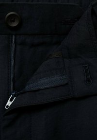 Pantalon en tissu noir doté d'une braguette zippée et d'une fermeture à bouton, avec une poche intérieure et une doublure lisse et texturée.