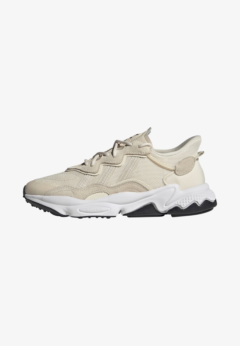 Beige athletic shoe featuring a mesh and suede upper, textured accents, a thick white midsole, and a black rubber outsole.