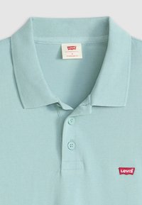 Light blue polo shirt made of textured fabric, featuring a three-button placket and a red Levi's logo on the chest. Standard fit design.