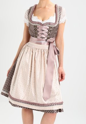 Vrouw die een bruine dirndl jurk met patroon draagt, een witte kanten blouse en een lichtroze schort, gestrikt in een strik in de taille.