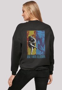 Schwarzer Sweatshirt mit einem bunten Grafikdesign auf der Rückseite, das eine Figur und den Text "NUTZE DEINEILLUSION" zeigt. Lässiger Schnitt, gerippte Bündchen.