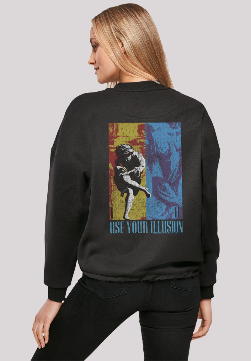 Schwarzer Sweatshirt mit einem bunten Grafikdesign auf der Rückseite, das eine Figur und den Text "NUTZE DEINEILLUSION" zeigt. Lässiger Schnitt, gerippte Bündchen.