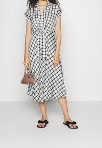 Černobílé kostkované midi šaty s krátkými rukávy, zavázaným pasem a splývavou sukní. V kombinaci s černými sandály s volánky a malou kabelkou.