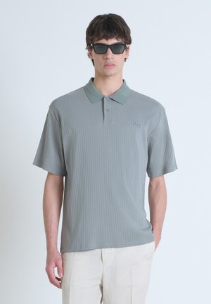 Polo gris con tejido acanalado y textura suave, de mangas cortas y con cuello. Presenta un pequeño detalle bordado en el pecho.