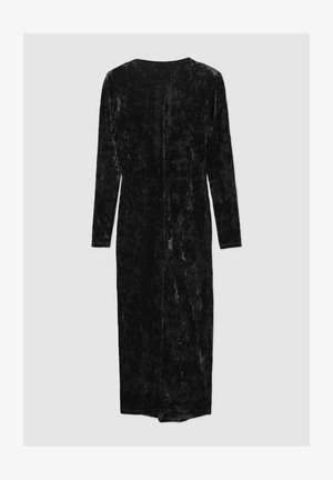 Robe en velours noir avec des manches longues, design jusqu'aux genoux et coupe droite. Présente un éclat subtil et une fermeture éclair au dos.