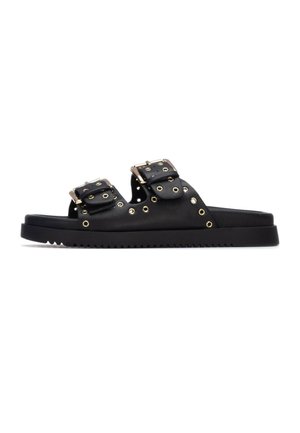 Sandalias negras con dos tiras ajustables con hebillas metálicas y ojales decorativos dorados, suela plana con dibujo texturizado.