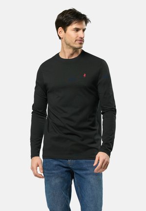 Camiseta negra de manga larga de algodón con cuello redondo, que presenta un pequeño logo rojo en el lado izquierdo del pecho, combinada con jeans azules.