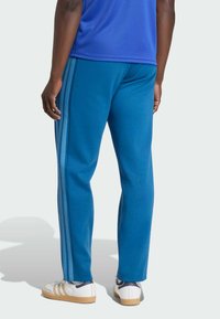 Modré športové nohavice z mäkkého materiálu, s bledomodrými bočnými pásikmi, voľného strihu, v kombinácii s bielou obuvou.