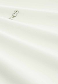 Witte stof met een gladde textuur en een lichte glans. Bevat subtiele plooien en een geprinte tekstlogo in een gedempte kleur.